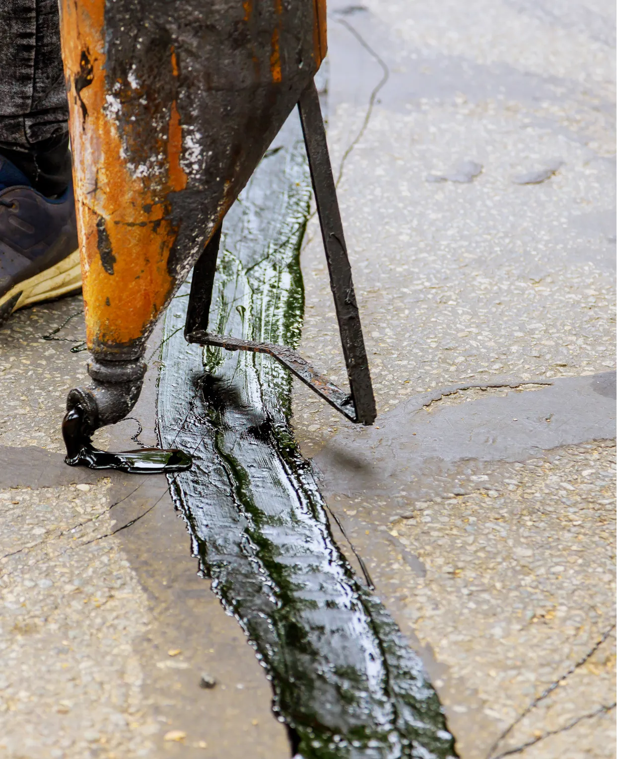 Close-up of a machine applying hot black tar to seal a crack in a paved road surface.