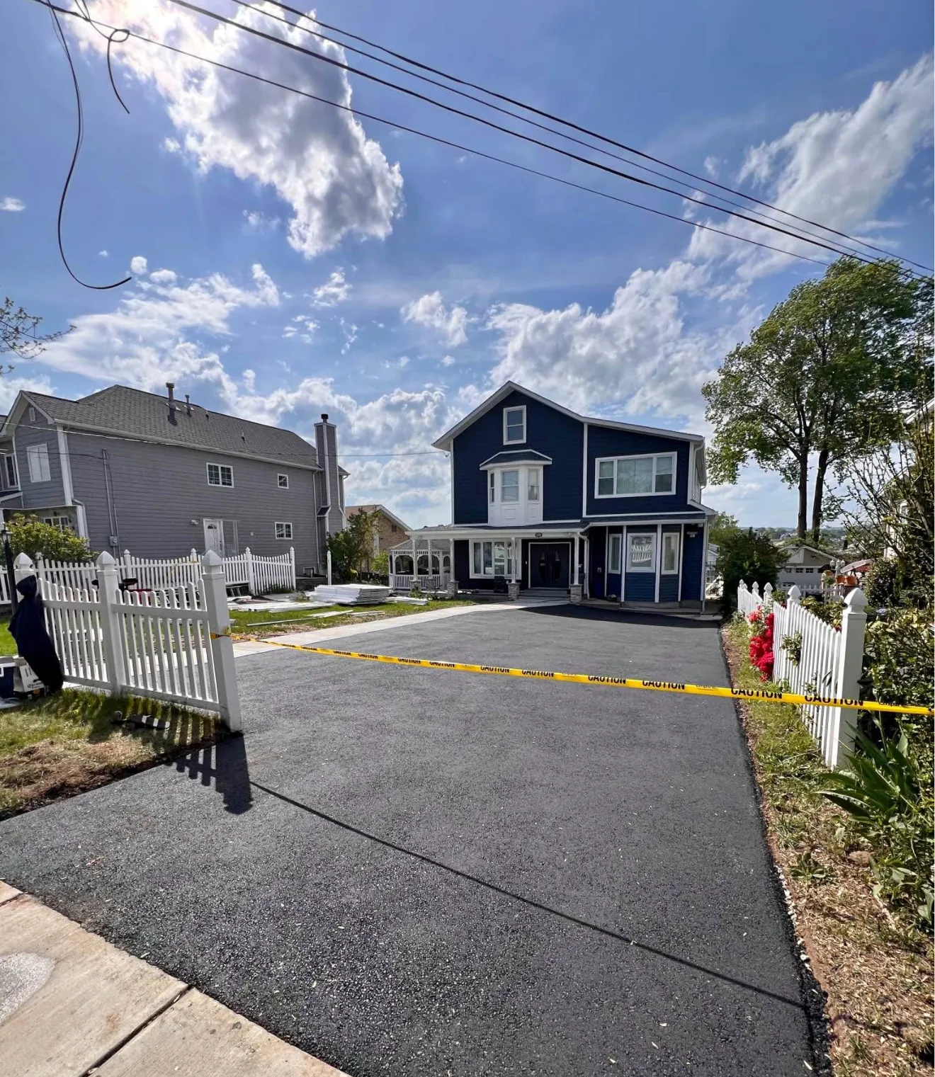 A newly paved driveway in front of a blue house, blocked off with yellow caution tape.