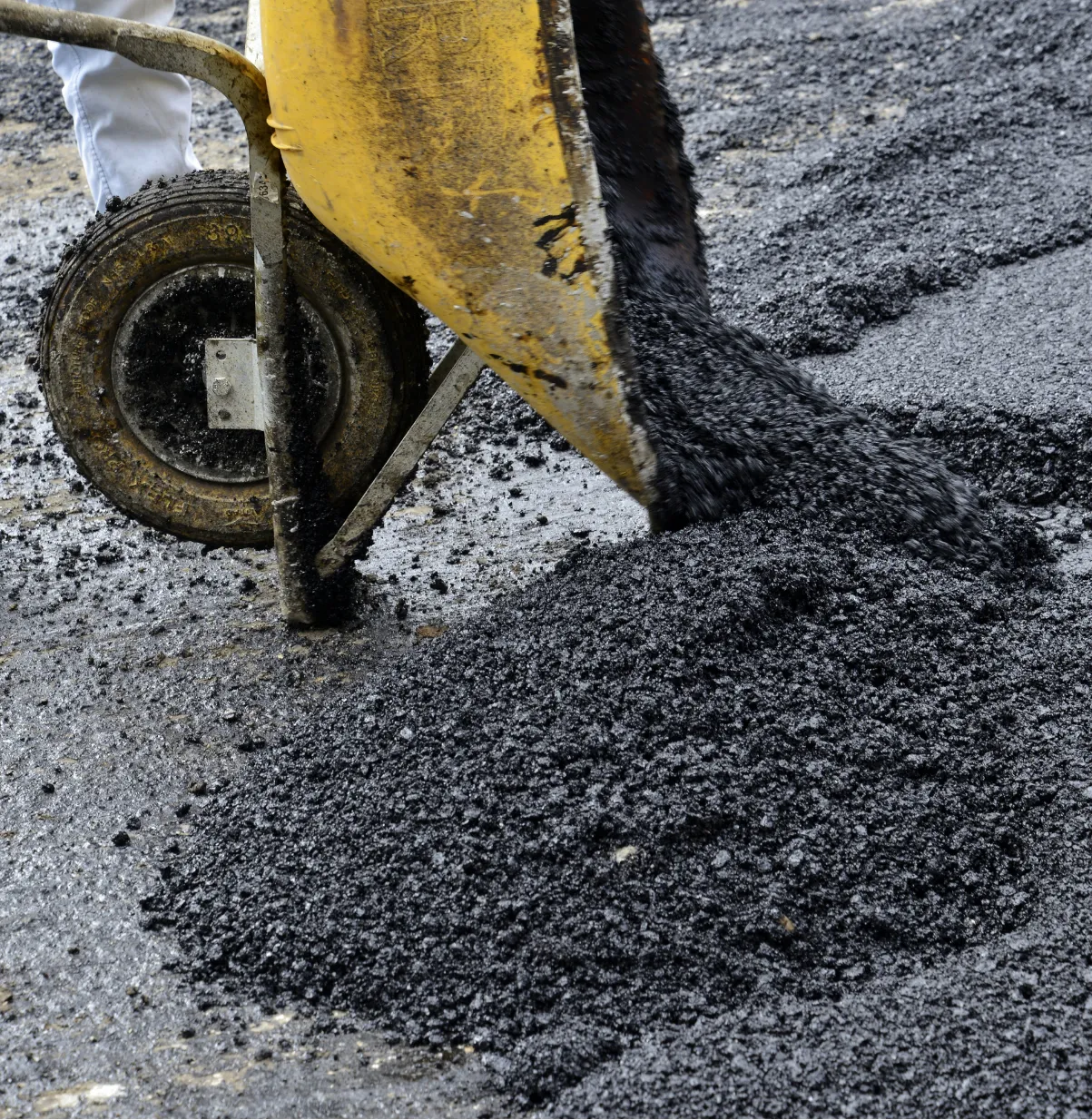 A wheelbarrow dumps fresh asphalt onto a road under construction.