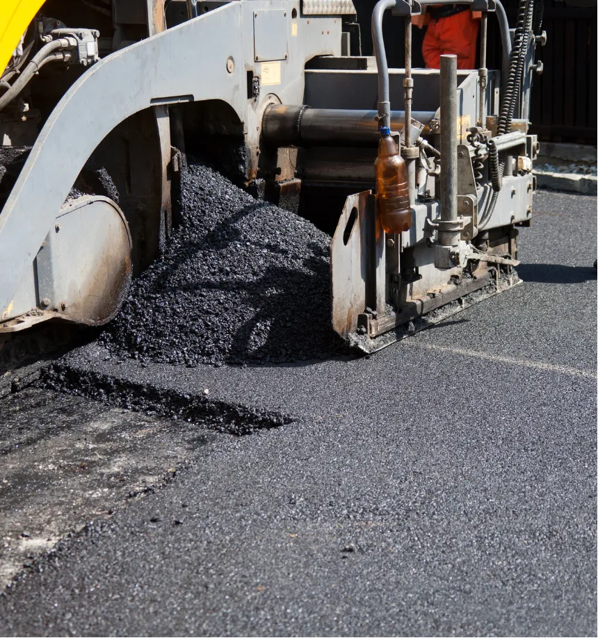 A road paving machine spreads fresh asphalt as workers resurface a street.