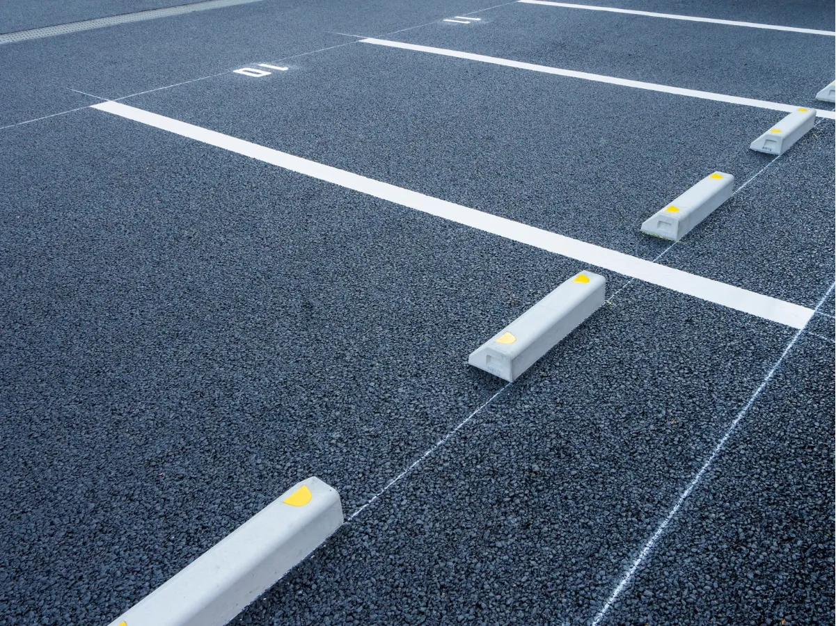 Empty parking spaces with white lines and concrete wheel stops on an asphalt lot.