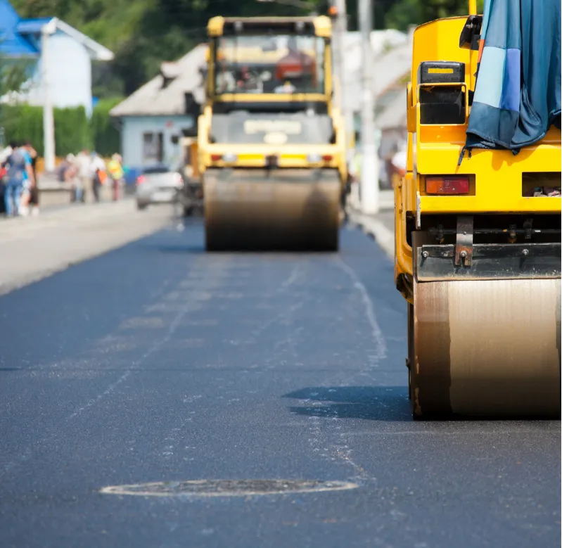 Close-up of road rollers paving fresh asphalt on a street in a residential area.