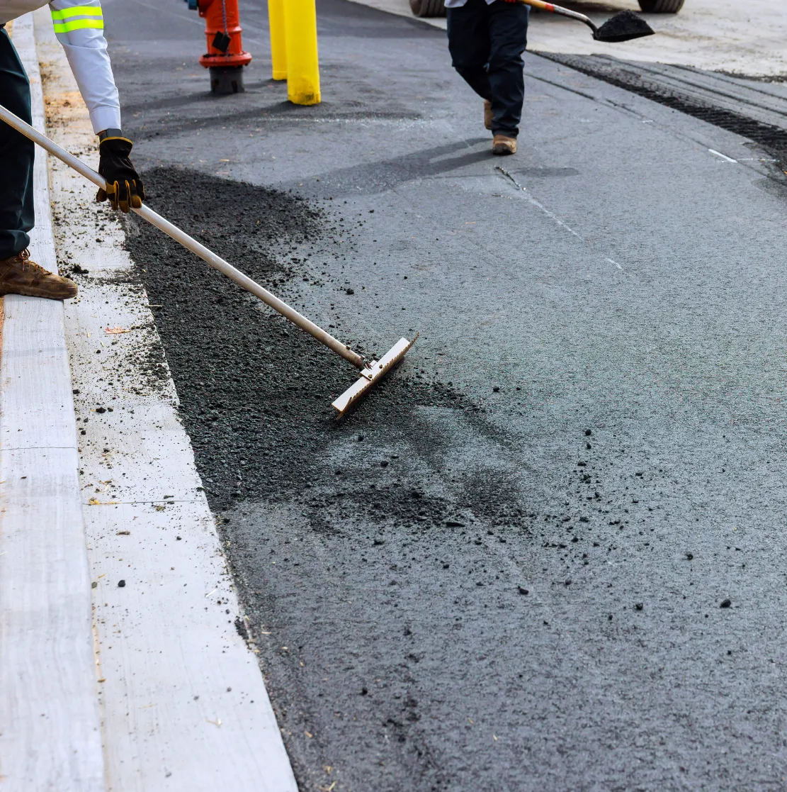 Workers spreading asphalt on a road surface with tools during street construction.