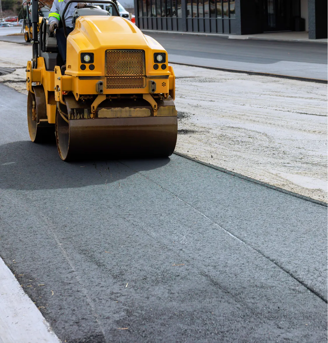 A yellow steamroller flattens fresh asphalt on a road under construction.