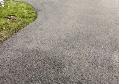 Freshly paved asphalt driveway with a worker using equipment and grass along the edge.