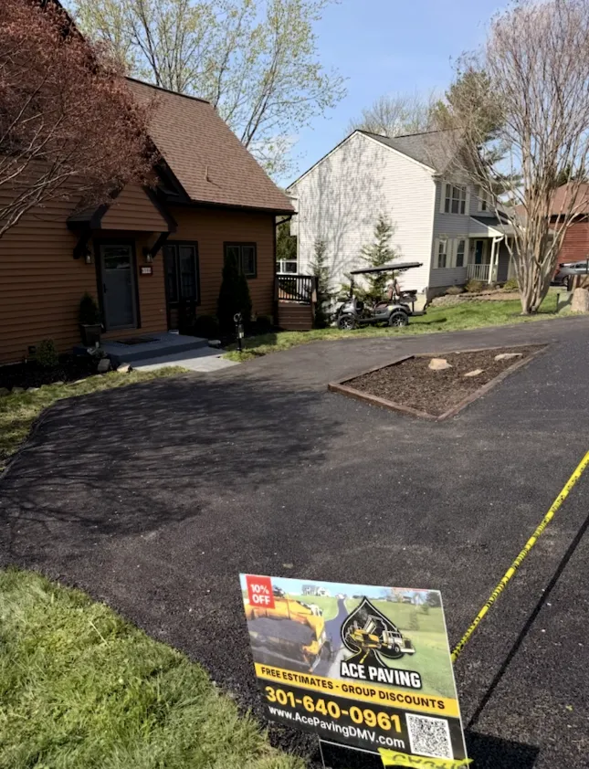 Freshly paved driveway in front of a house with an Ace Paving sign and construction tape in the yard.