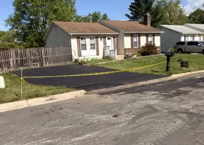 Single-story house with freshly paved driveway, blocked off by yellow caution tape on a sunny day.