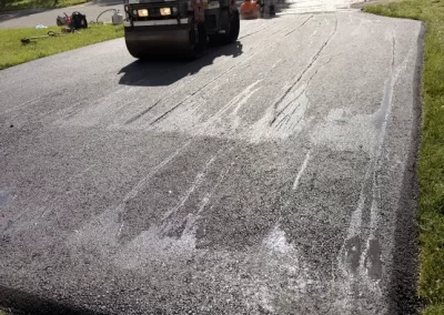Workers paving and smoothing fresh asphalt on a driveway in a residential neighborhood.