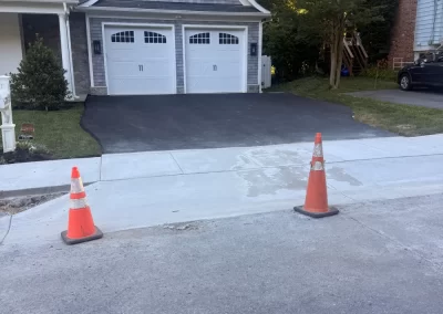 Two orange cones block the entrance to a driveway with fresh black asphalt in front of a house.