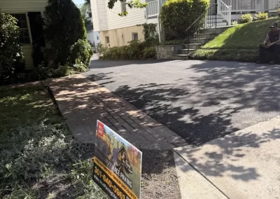 A driveway with a landscaping company sign in front of a house with an American flag.