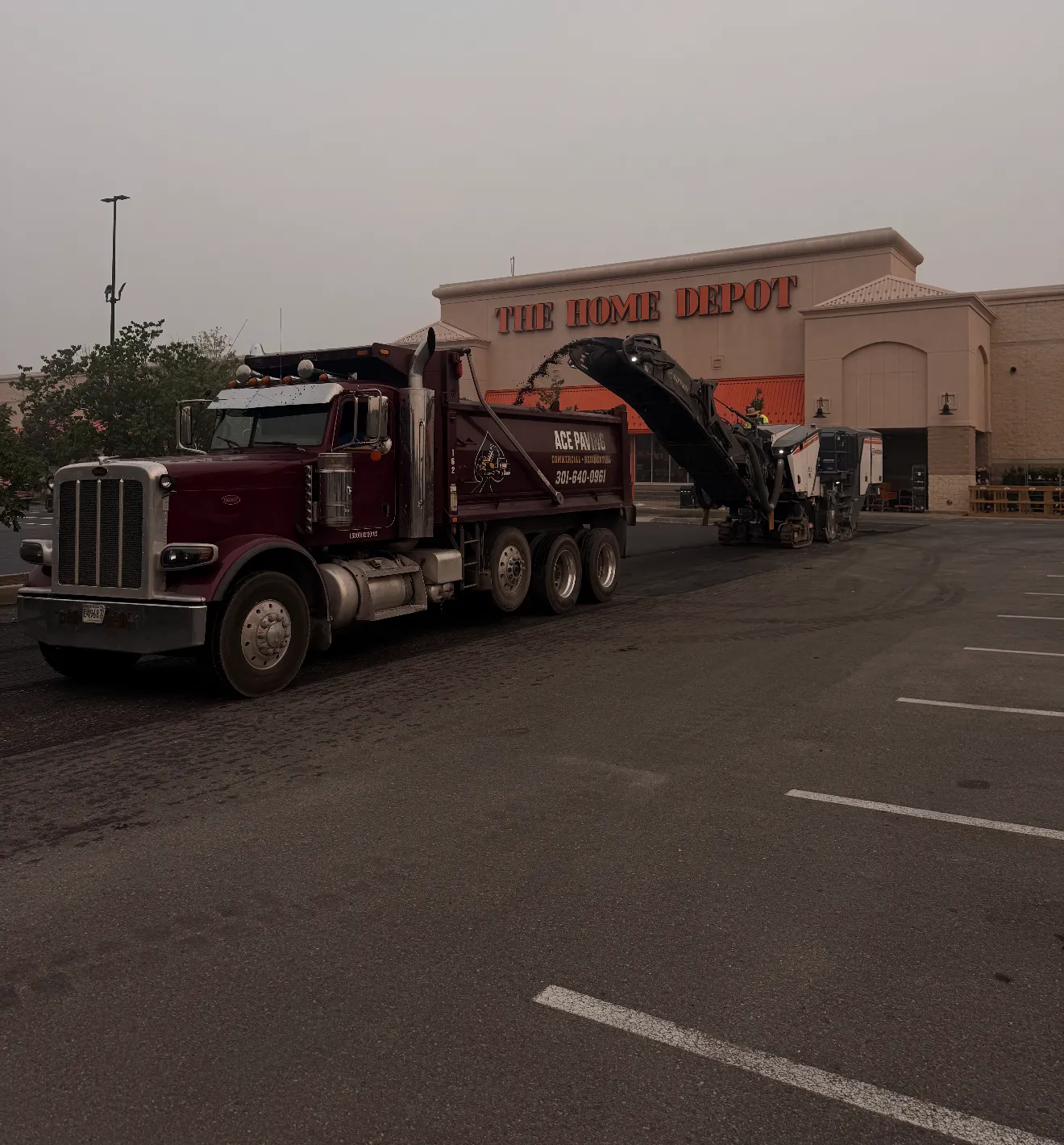 A dump truck and roadwork equipment are parked in front of The Home Depot on an overcast day.